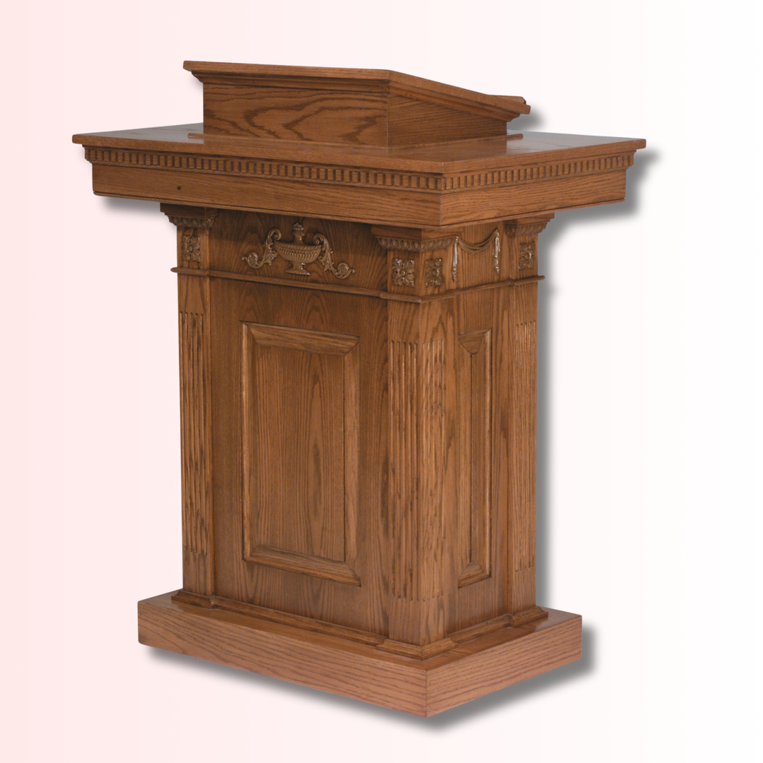A wooden pulpit with a warm medium-brown finish, featuring decorative carved details on the upper panel and a slanted lectern top, shown against a light pink gradient background.
